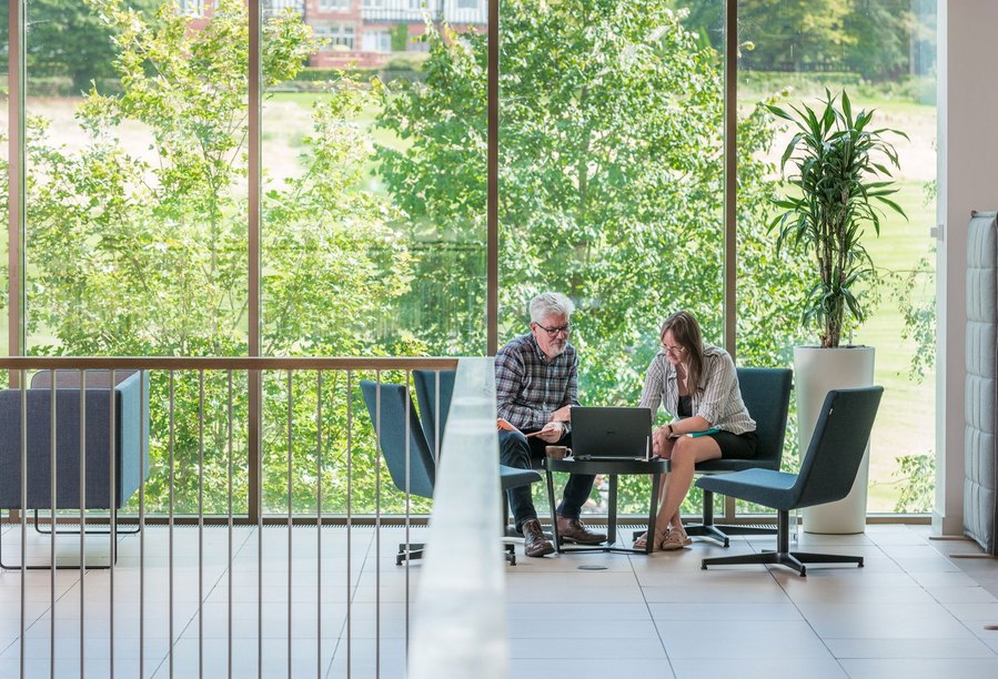 Two people in a modern office space with large windows overlooking green trees.