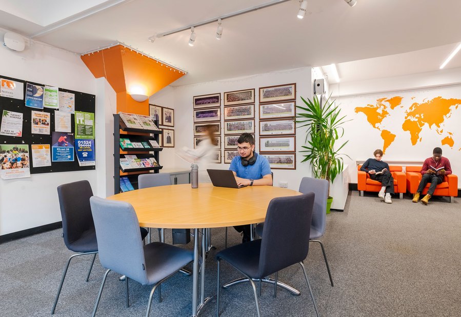 student lifestyle photography, student sits in room with colourful wall murals working on a laptop