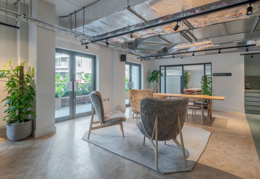 Modern office lounge area with stylish chairs, wooden floor, and exposed ceiling ducts.