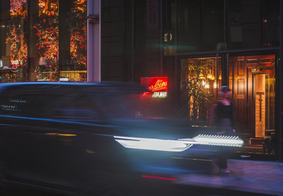 URBAN LIFESTYLE AND LOCAL AREA PHOTOGRAPHY OF SPINNINGFIELDS, MANCHESTER, night time lifestyle shot of blurred car passing a neon sign and person walking past