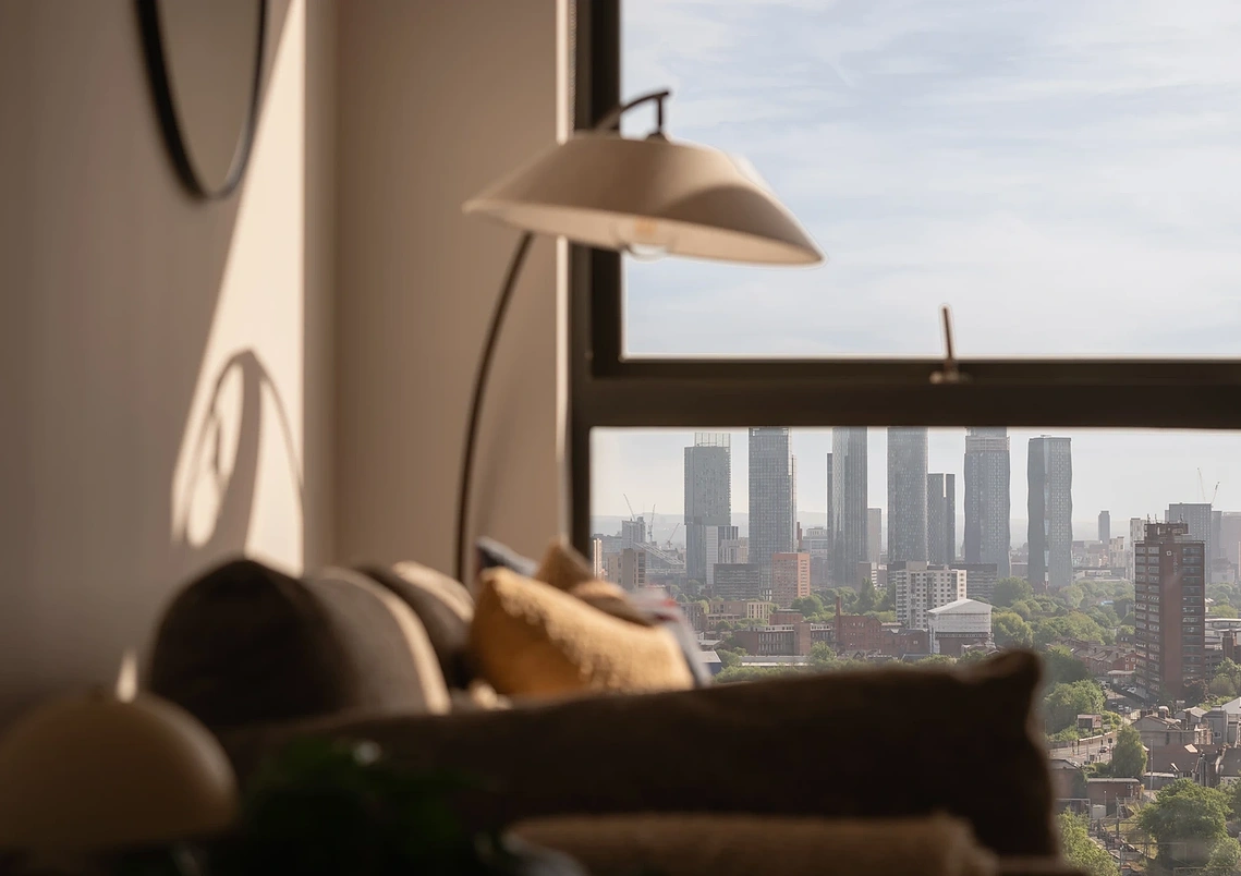 Manchester city centre skyline from a Podium apartment window, with a soft-focus sofa and floor lamp