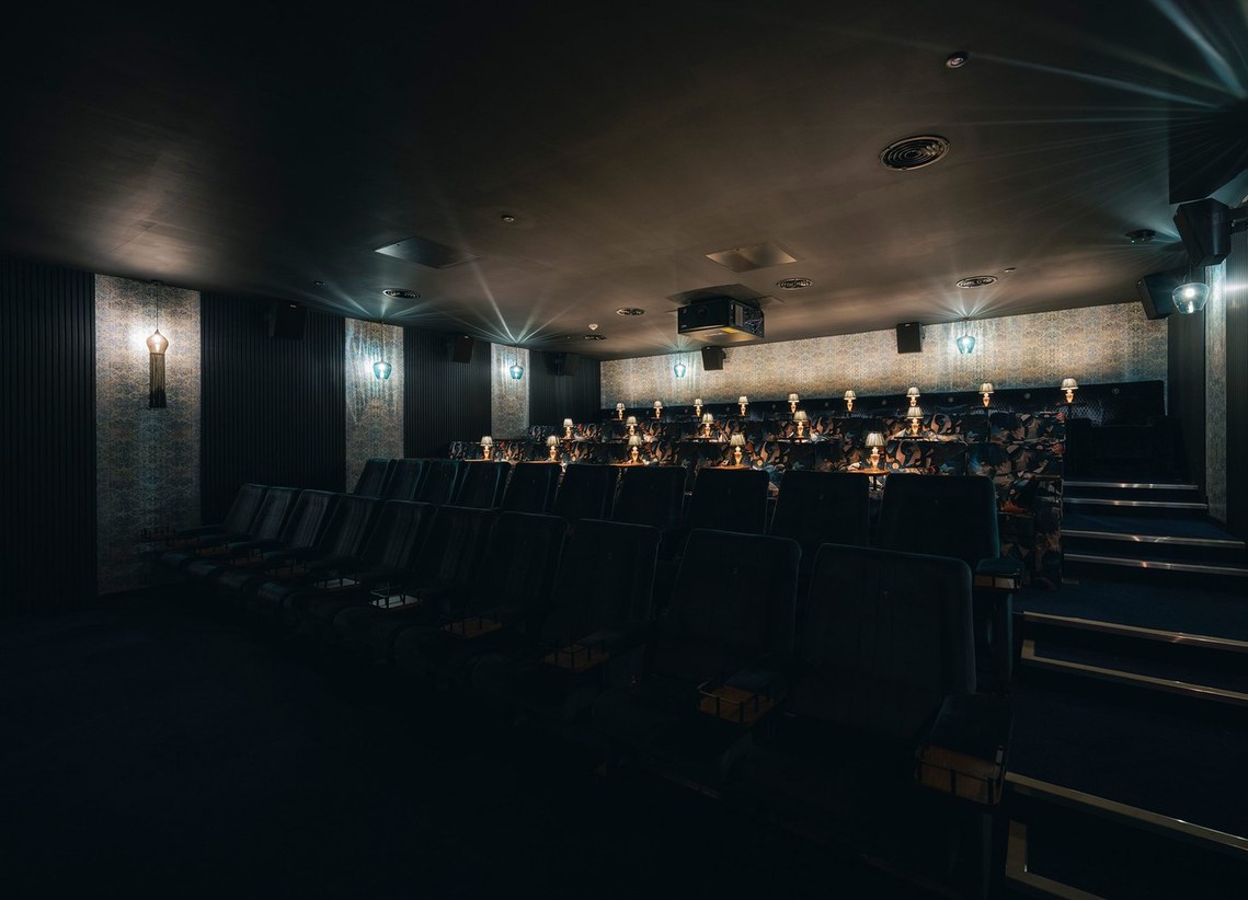 wide photograph of cinema auditorium, with boutique seats and table lamps