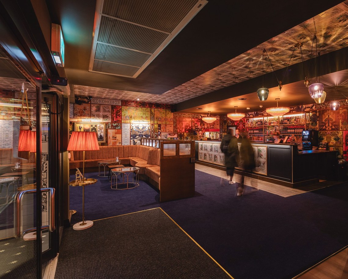evening shot of cinema lobby with glowing red lights and colourful decor. customers walking toward desk