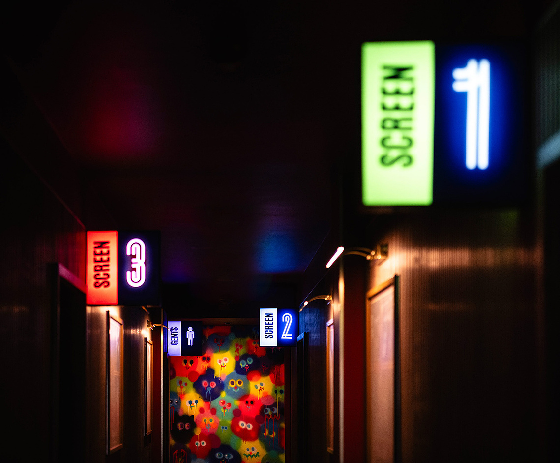 cinema corridor with glowing signs showing screen numbers and colourful mural on wall