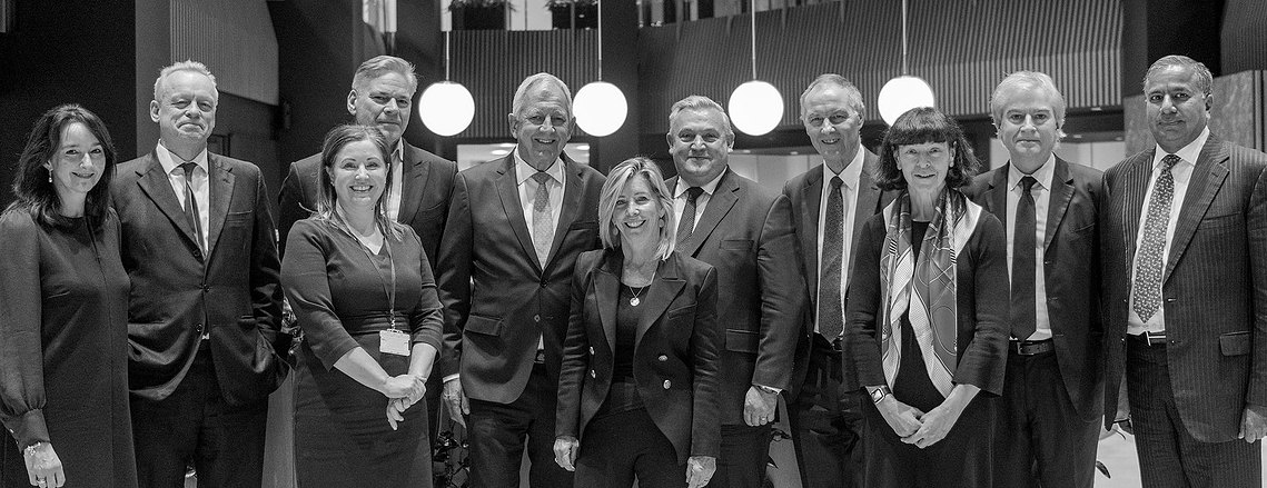 A group of ten people in formal attire stand together in a room with round overhead lights, perfectly captured by a Manchester commercial photographer known for relaxed corporate photography.