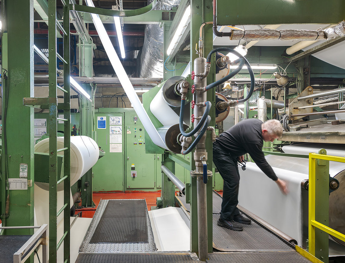 Documentary manufacturing photography capturing a factory worker operating machinery and ensuring quality.