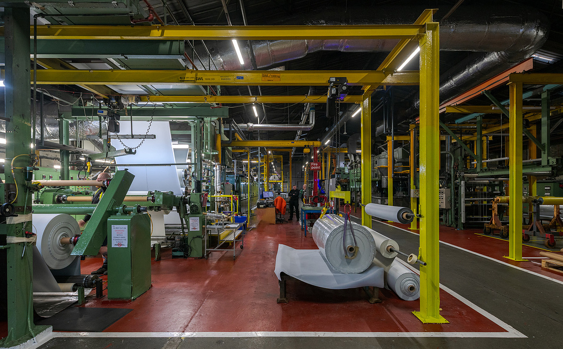 Industrial interior photography showing colourful machinery and large rolls of vinyl-coated fabrics inside a factory in Lancashire
