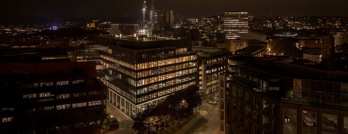 modern building lit up at night, elevated angle from a drone, bristol city in background