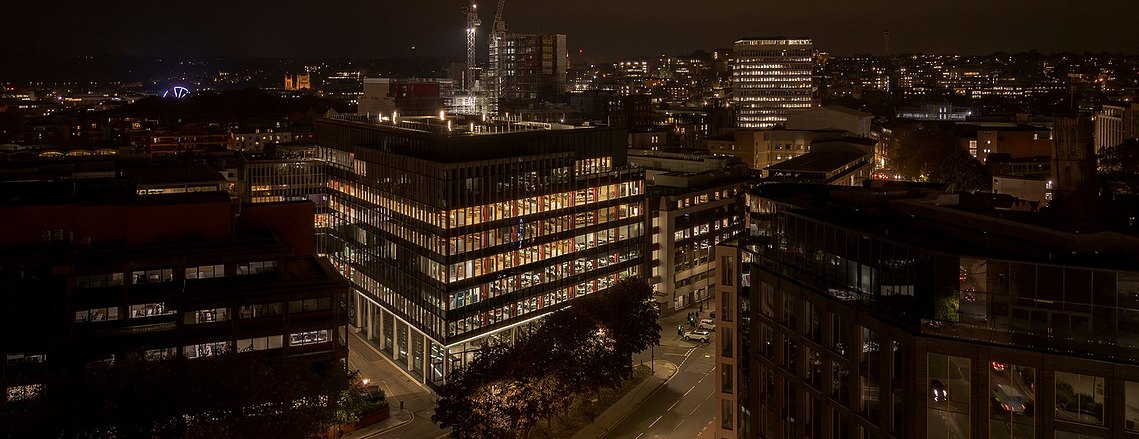 modern building lit up at night, elevated angle from a drone, bristol city in background