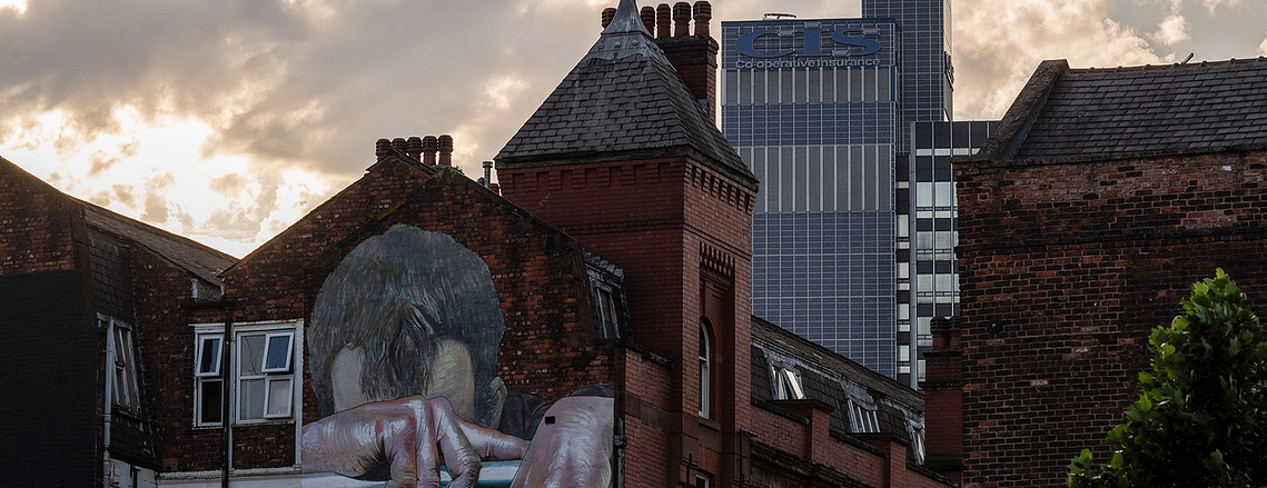 Placemaking architecture photography showing the CIS Building rising above Manchester’s everyday street life. Evening light and street art in foreground