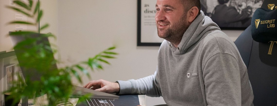 person in a home office, sat looking at screen and smiling as they chat with colleagues