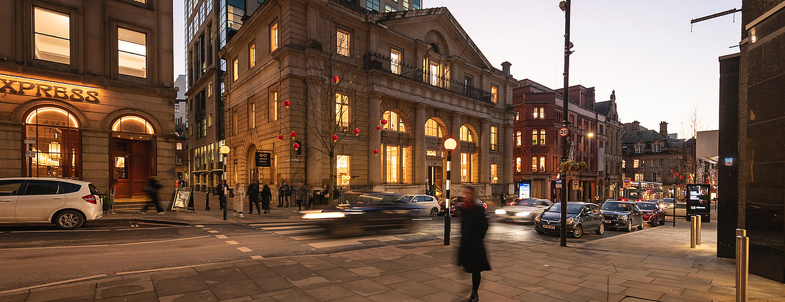 street scene at dusk, period style building in Manchester City centre, with cars and walkers blurred