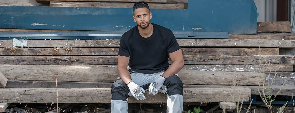 On-location brand photoshoot for ProDec , shows model in workwear sat in industrial setting
