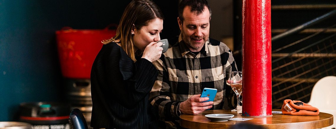 stockport lifestyle photography, customers sitting at table inside a cafe looking at phone 