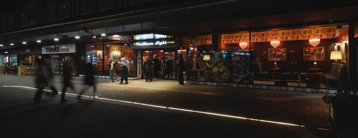 exterior architecture photography of boutique cinema. front of cinema at night. lit up from inside. blurred people walking out of the door