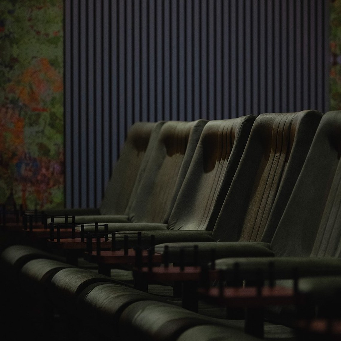 cropped photo of green luxury cinema seating, with ornate colourful wall coverings and drink holders on the chairs