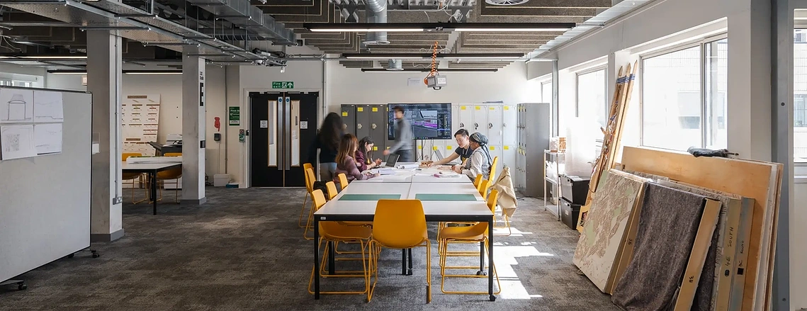 Group of architecture students collaborating over floor plans at a large studio desk