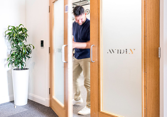 Man walking through an office door made of glass with company name on the glass. plant behind door
