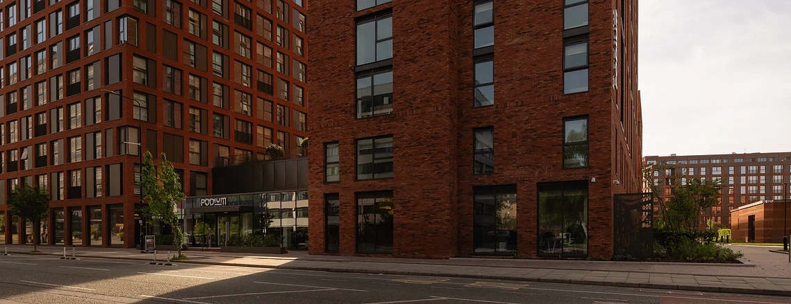 Street-level view of Podium's red brick towers and entrance in Old Trafford, Manchester. Architectural property photography.