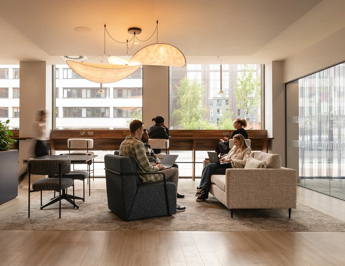 Residents on laptops beneath sculptural pendant lights in Podium's co-working lounge, Old Trafford, Manchester.