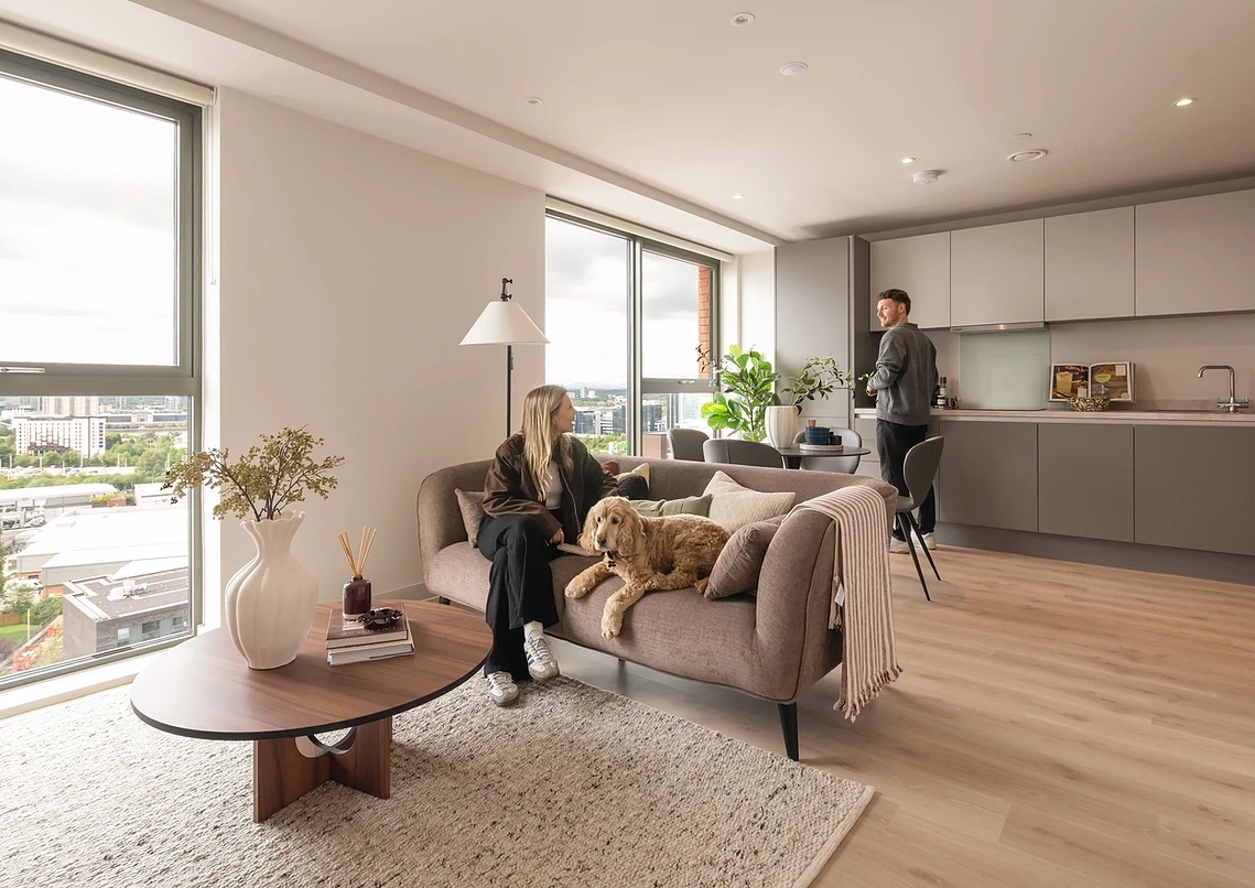 Couple and their dog relaxing in Podium's show apartment, with floor-to-ceiling windows over Old Trafford, Manchester.