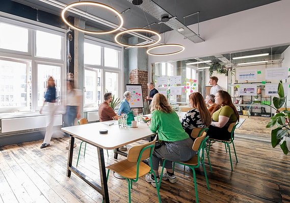 Commercial lifestyle photography of a modern workplace and specifically a meeting room. Workers around a table and some walking around.