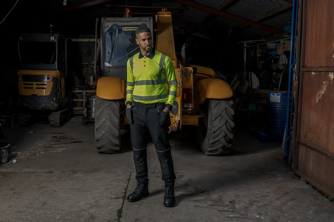 Workwear product photography showing PPE in an industrial setting, model in bright workwear poses in front of machinery