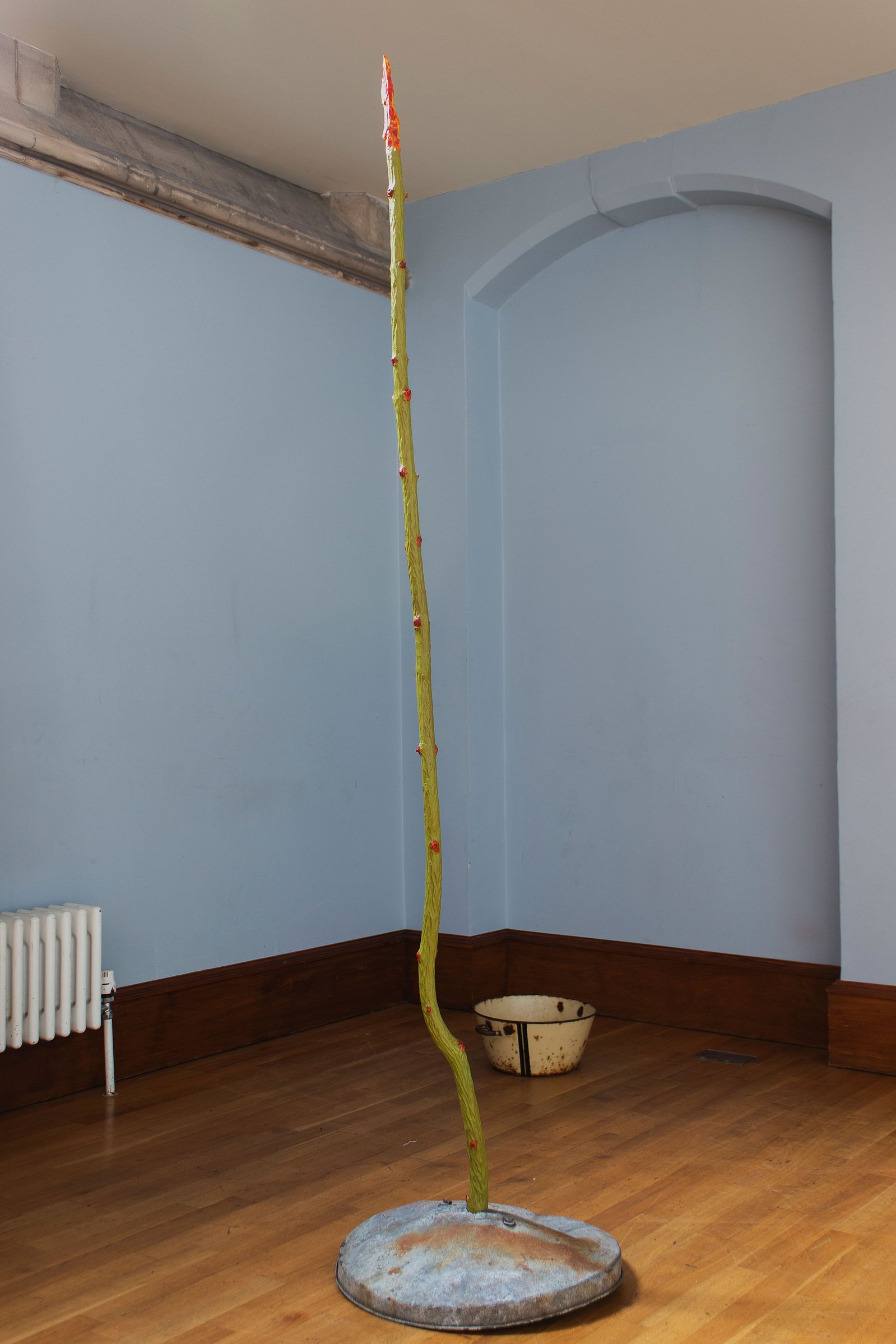 Carved wooden sculpture painted green and orange with metal base. Blue walls. Jamie Kane