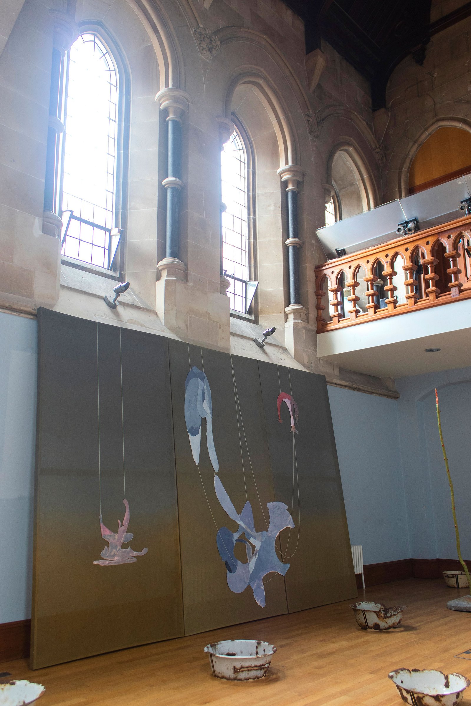 Painting canvas with paper objects and green fabric in a blue room. Church windows above. Jamie Kane