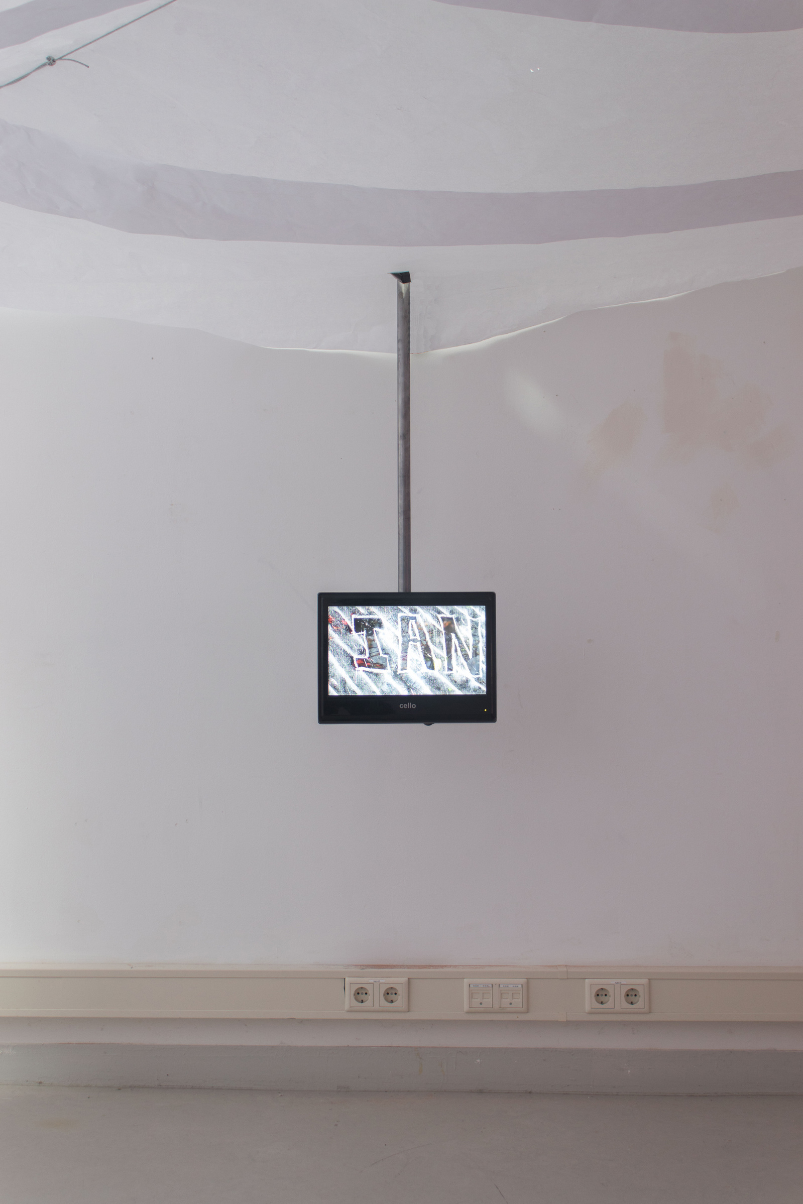 A room with paper ceiling. There is a video monitor on to behind coming down from the ceiling. On the monitor is reads the name Ian . Jamie Kane