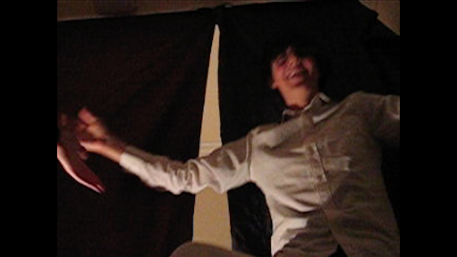 A smiling man wearing all white looking down. With a black curtain behind. Jamie Kane
