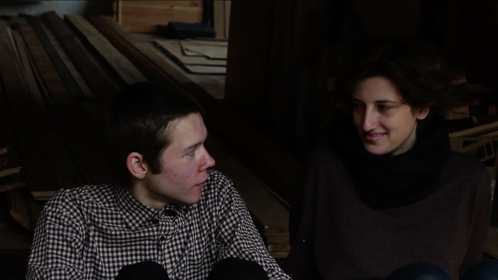 An image showing a male and female sitting facing each amongst some slats of wood