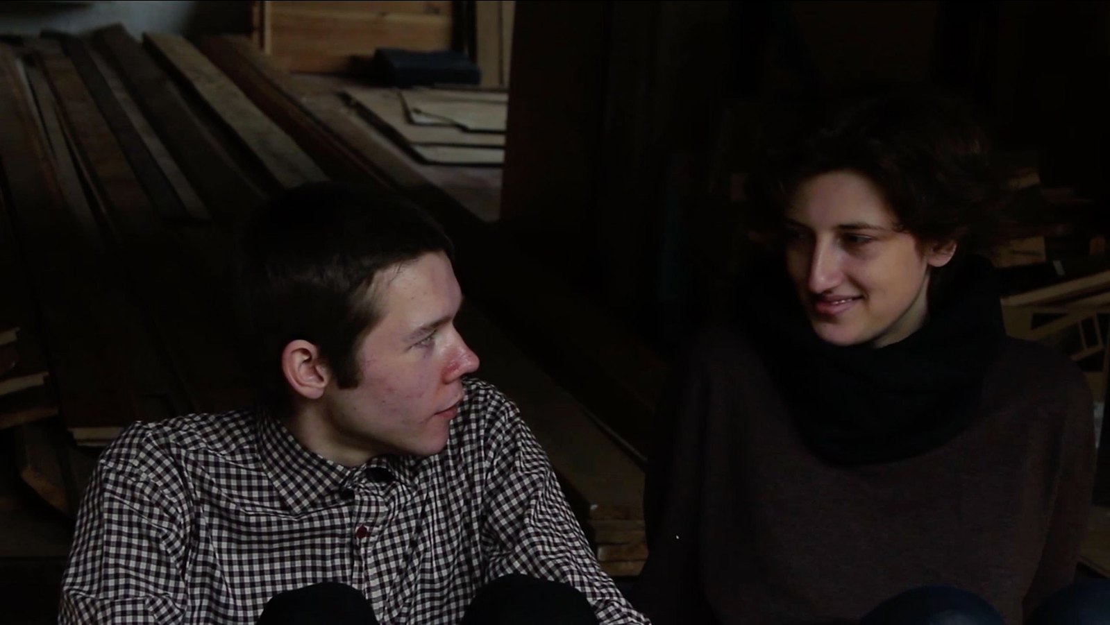 An image showing a male and female sitting facing each amongst some slats of wood