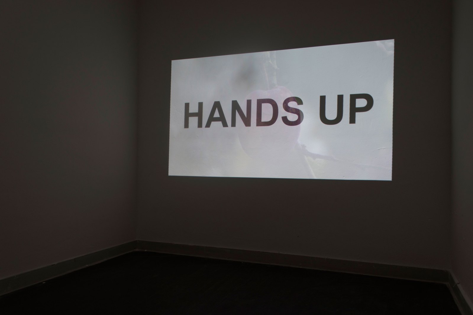 A projection in a dark room with the words 'hands up' seen projected. Jamie Kane