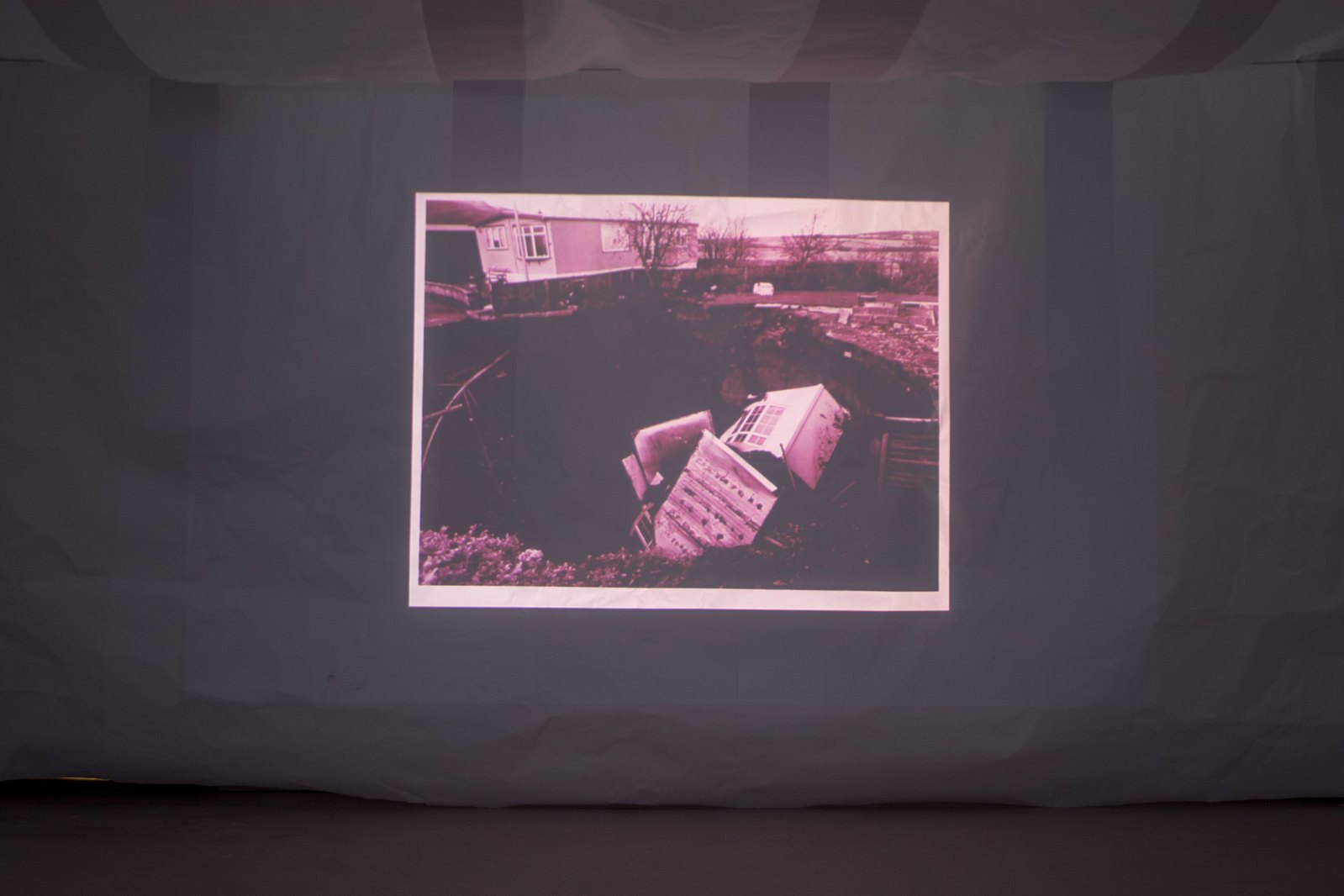 Projection onto paper showing a purple tinted photograph of a building into a sinkhole. Jamie Kane