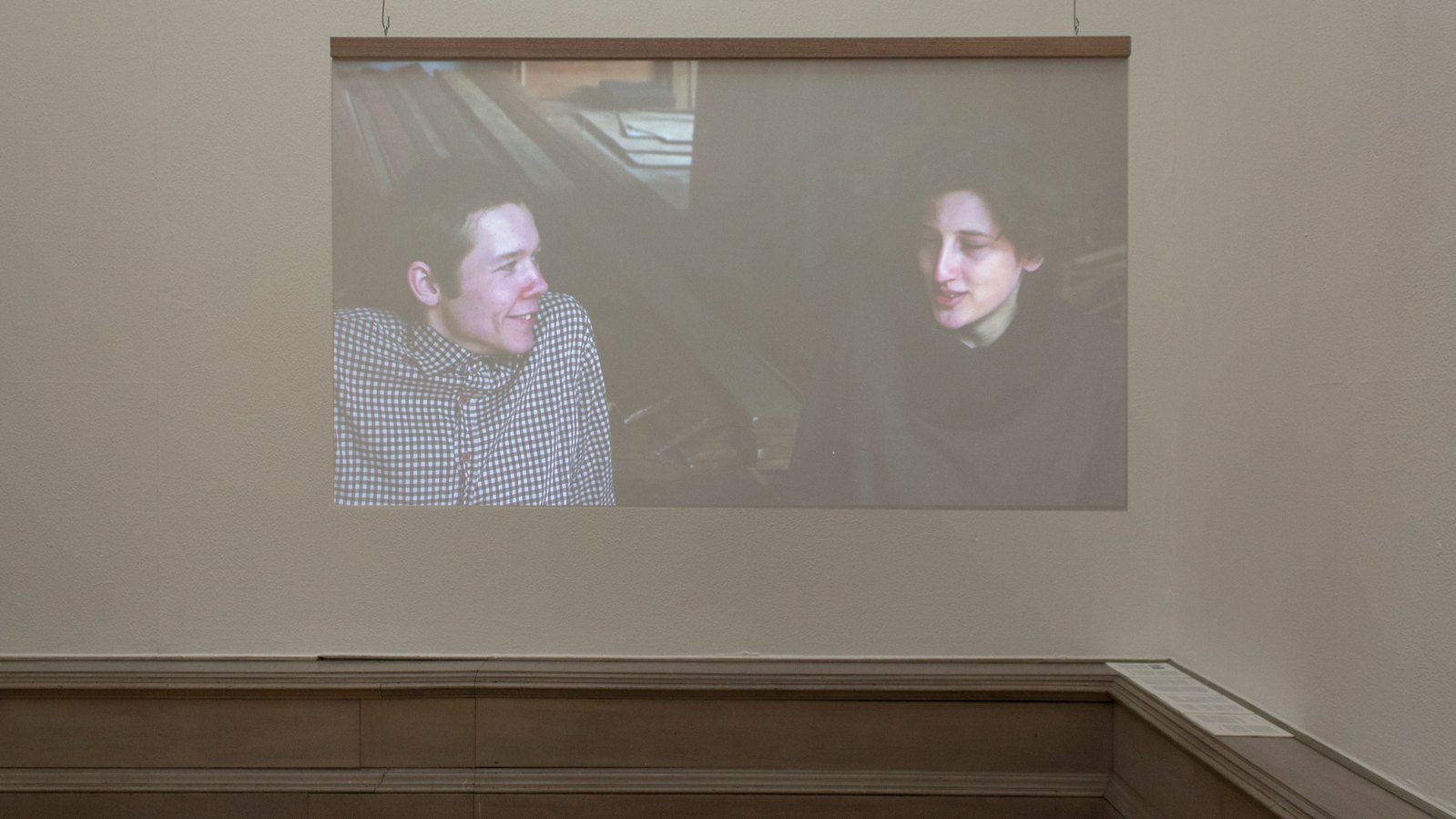 A Projection onto perspex sheet showing a male and female sitting facing each amongst some slats of wood