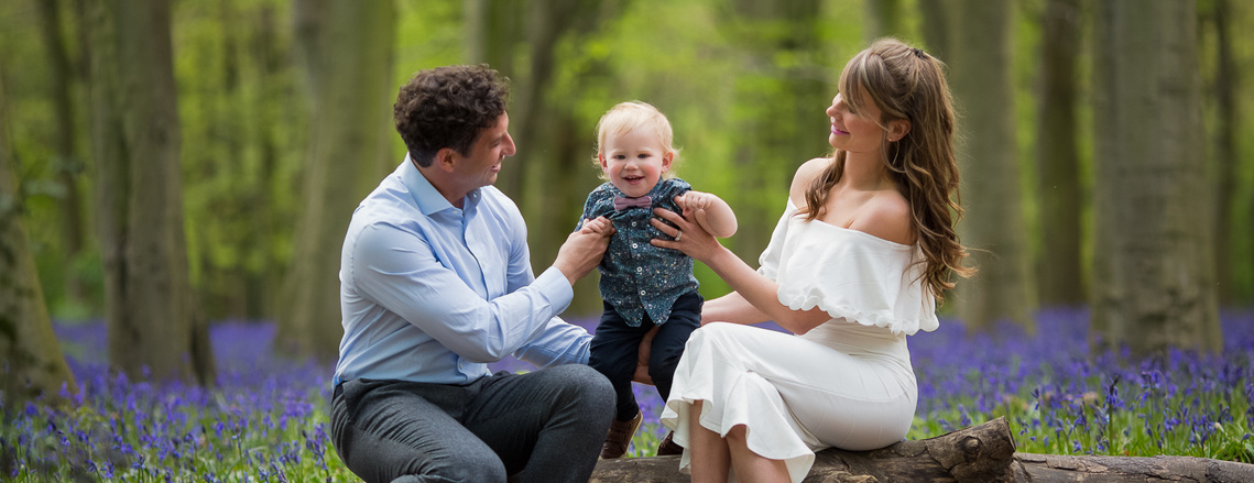 Family during a Bluebell Mini session in North East London seating among the bluebells. Little Bunny Photography - Maternity Child and Family Photographer in Woodford Epping Wanstead London. #bluebellphotoshootLondon #bluebellminisessionLondon