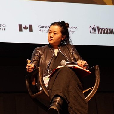 Abby Sun, wearing a leather jacket and a long dress, is sitting in a director's chair. Photo by Shevan Bastianpillai, courtesy of World Records