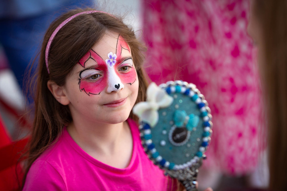 Child looking in mirror at painted face at family fun day event