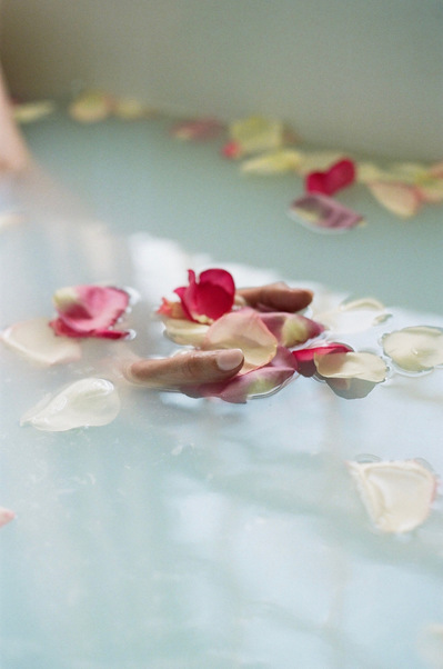 Hands holding delicate flower petals floating in milky bathtub