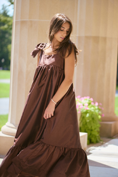 brunette model wearing rich brown satin silk maxi dress with stone columns behind her