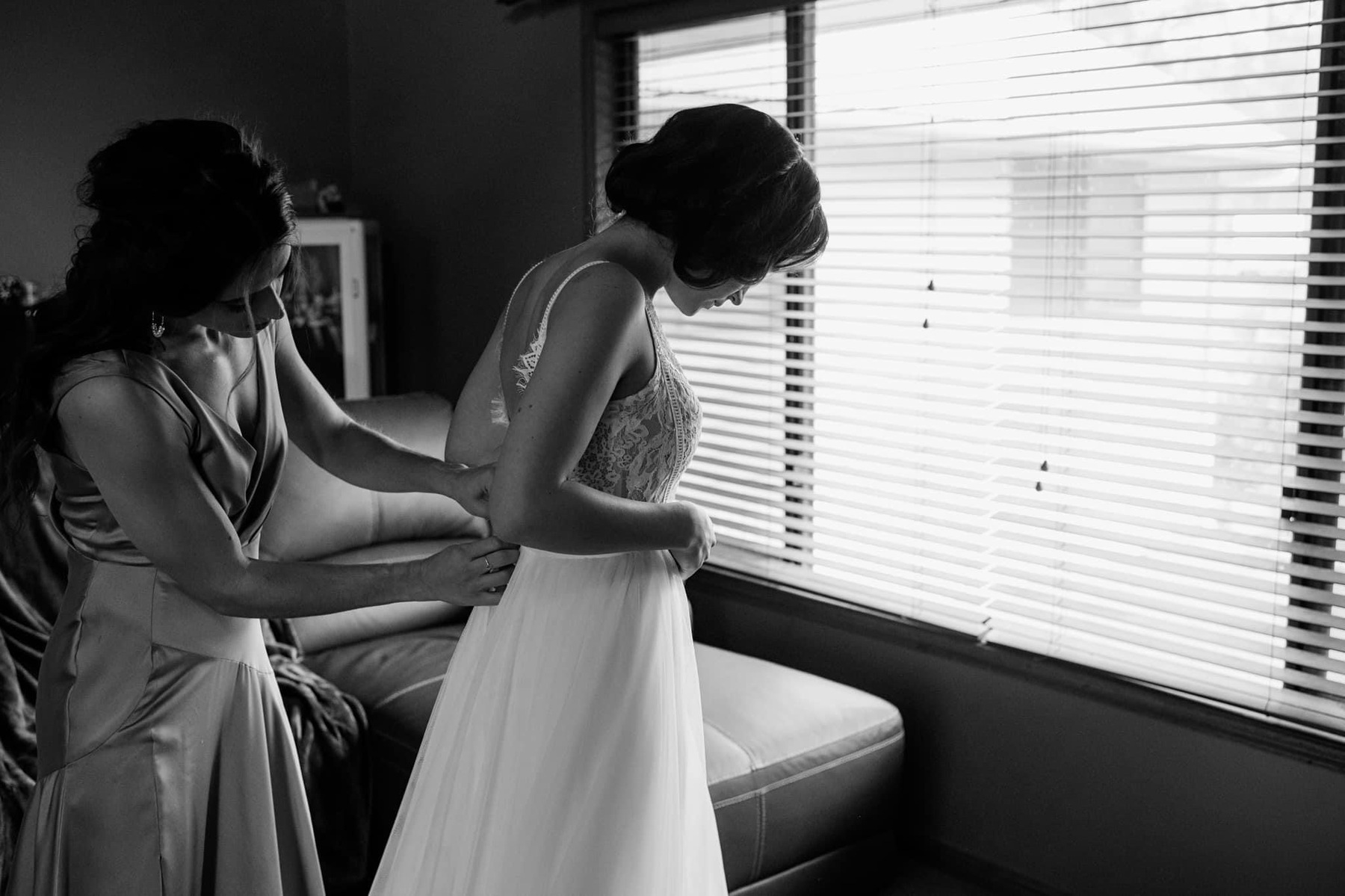 Black and white image of brides sister helping bride into her wedding dress. 