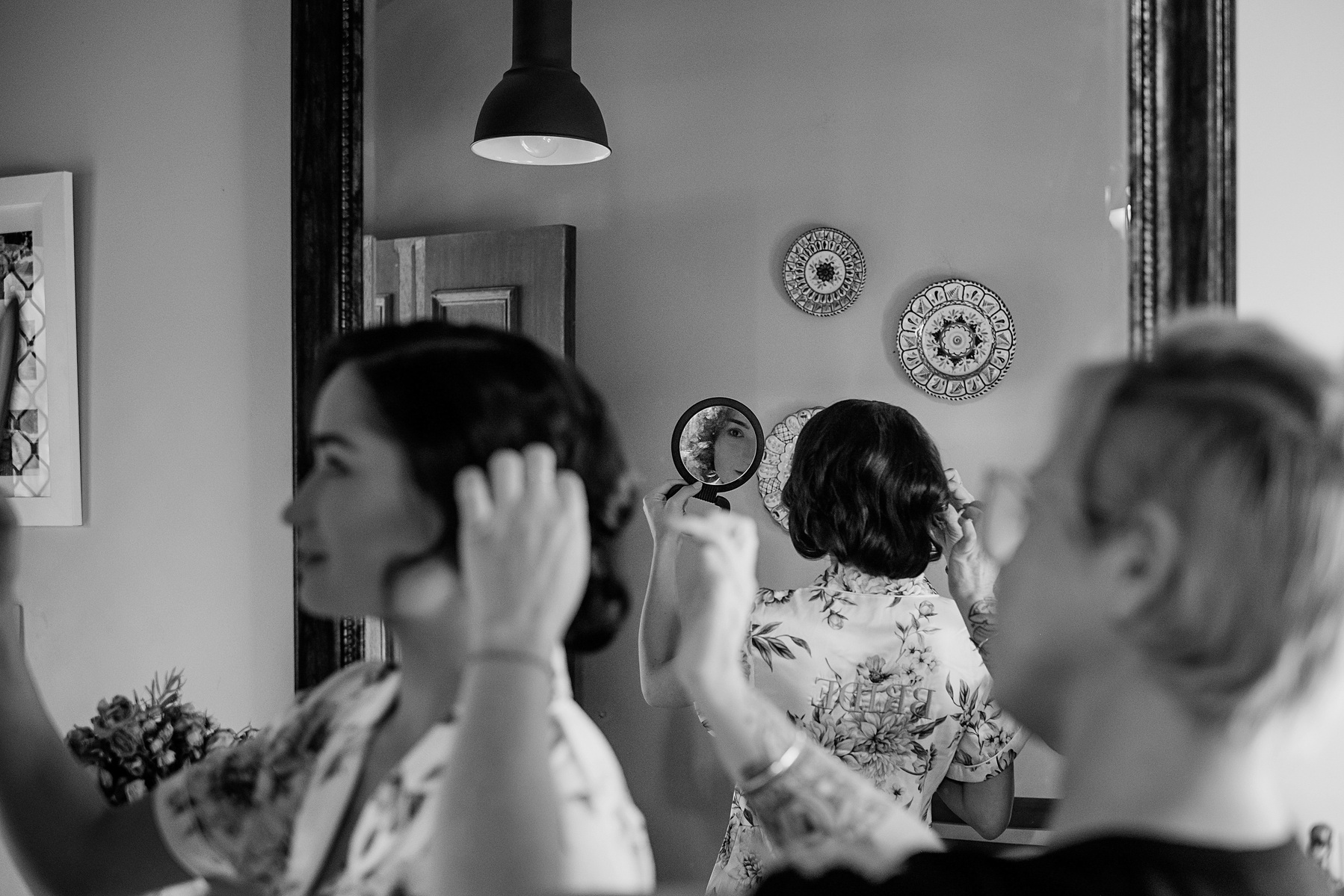Black and white image caught in the mirrors reflection. Hairstylist, Carly Stone making adjustments to a brides hairstyle.