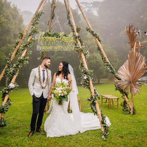 Bride and groom standing under adorned tee pee in misty mountain setting.