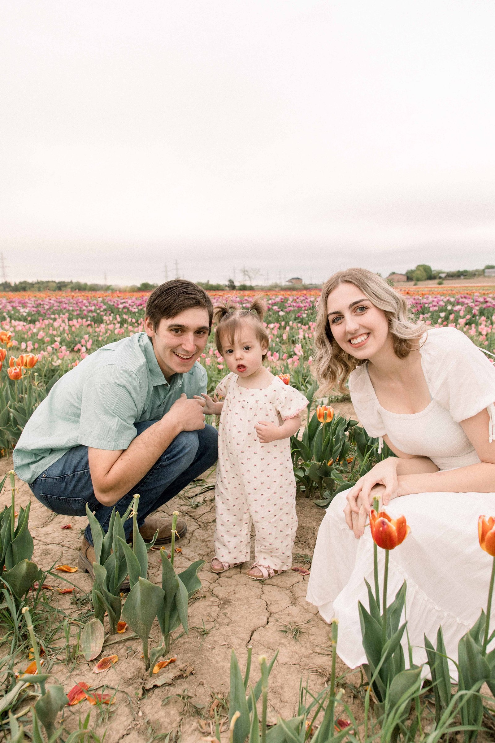 Portrait of a family of three at a tulip field in Niagara. Niagara portrait photographer. Niagara family photographer. Niagara photographer. Emily VanderBeek Photography. Candid photography. Light and airy photography