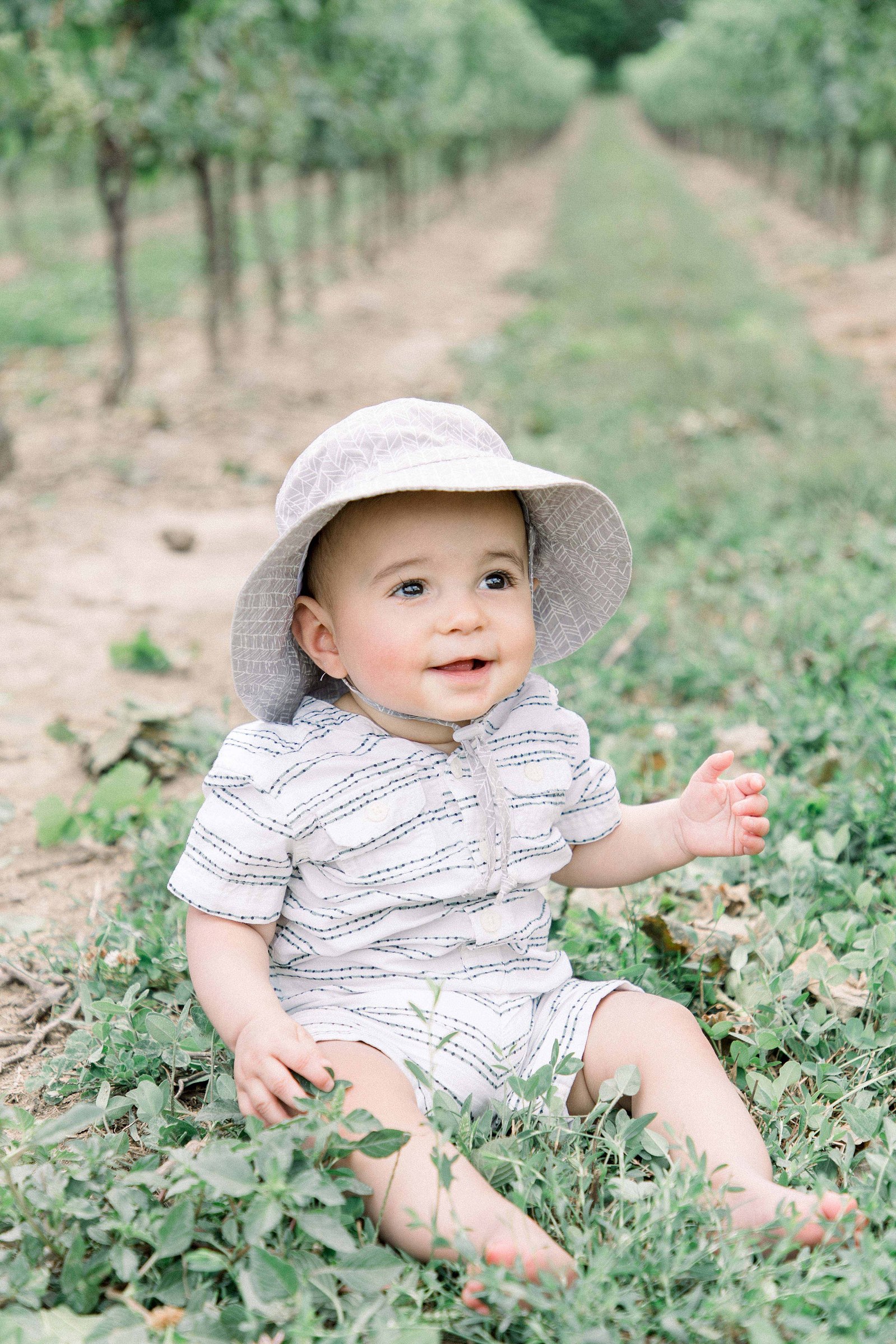 Portrait of baby boy sitting in a vineyard, looking into the distance. Niagara family photographer, Niagara family photography, Niagara portrait photographer, Niagara portrait photography.