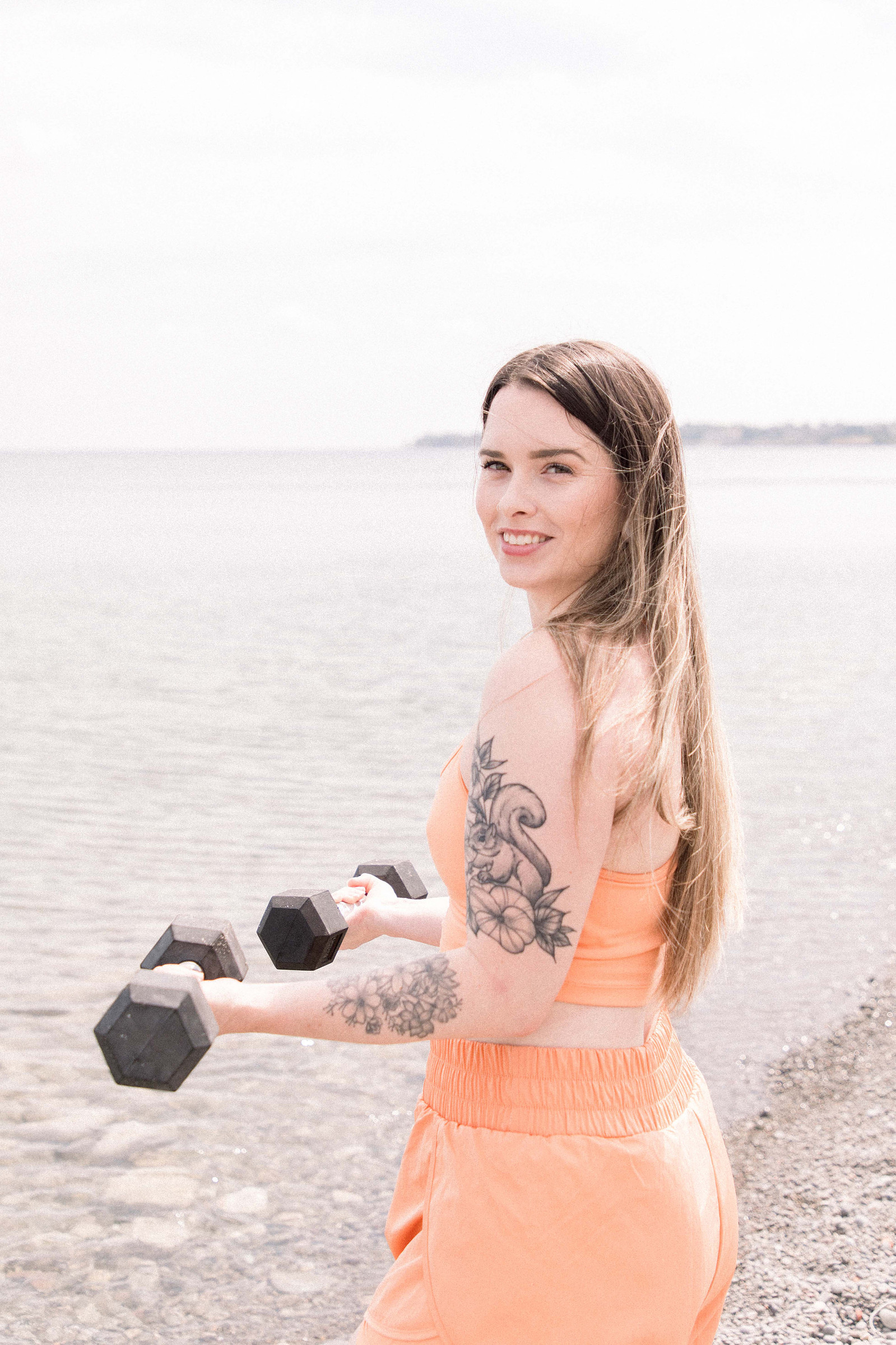 Portrait of young woman posing with dumbbells on the beach. Niagara family photographer, Niagara portrait photographer, Niagara motherhood photographer, candid photography, light & airy photography, Emily VanderBeek Photography.