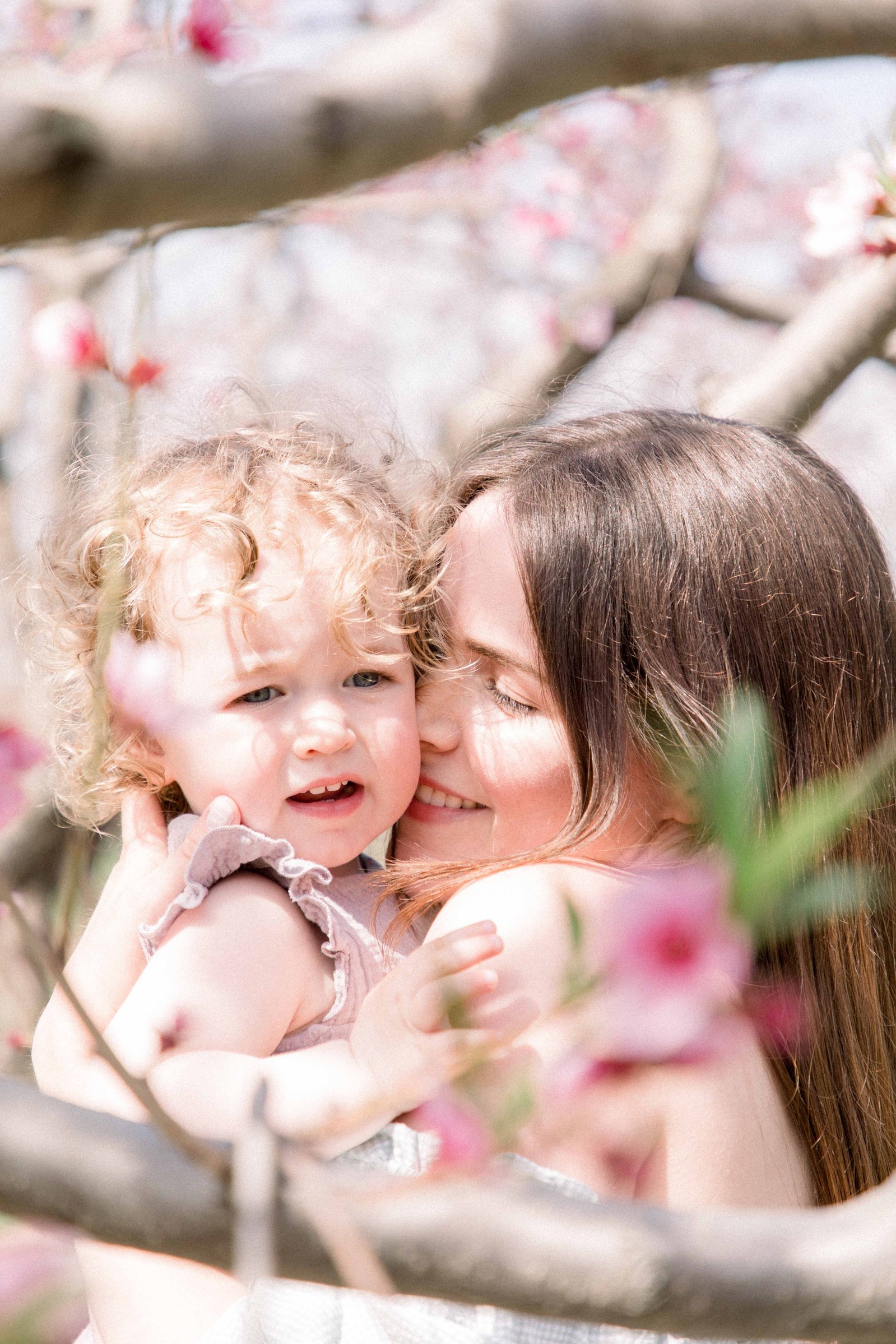 Portrait of mother and baby daughter hugging in an orchard of fruit blossoms. Niagara Family Photographer, Niagara Portrait Photographer, Niagara Motherhood Photographer. Emily VanderBeek Photography, Emily VanderBeek Photo.