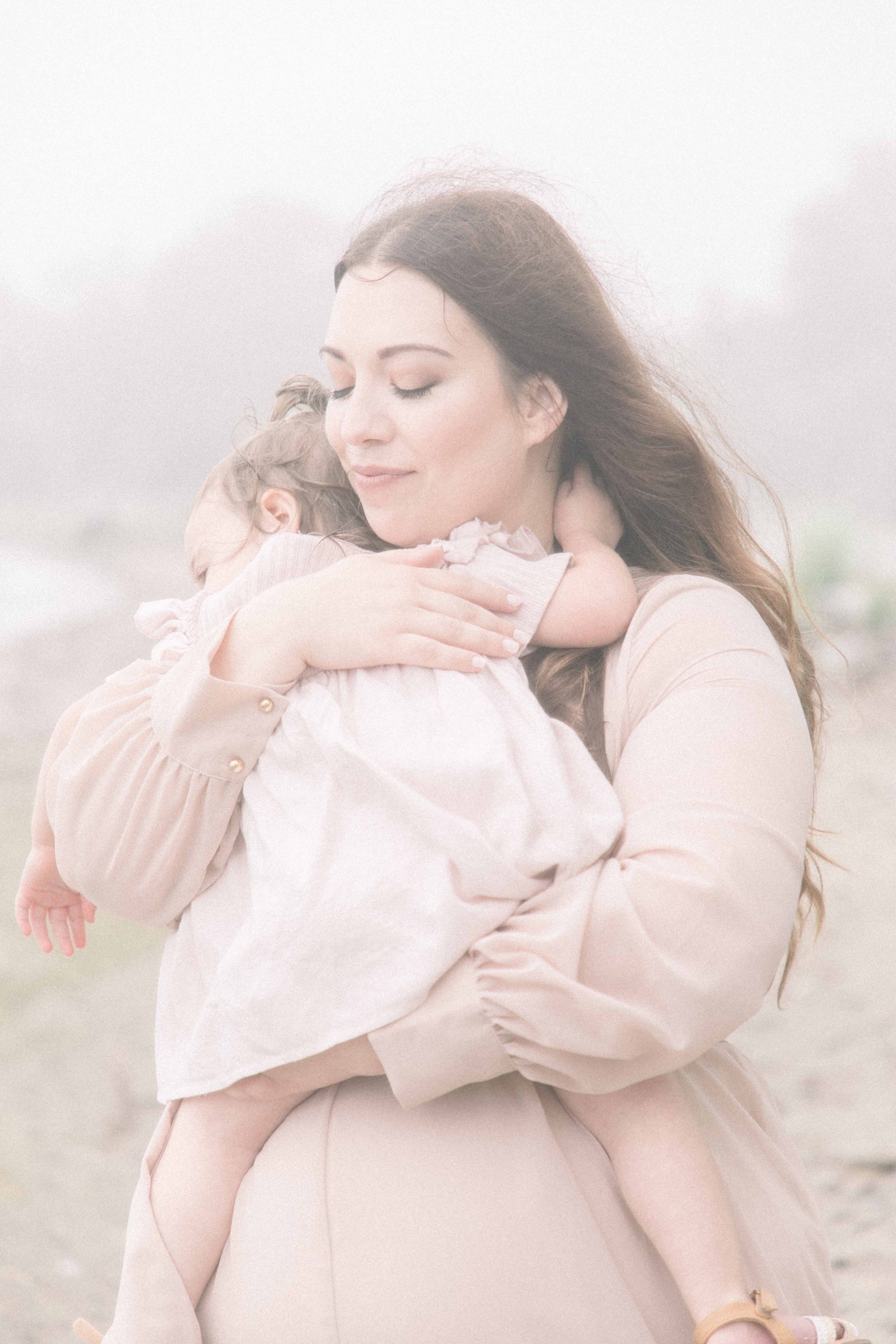 Portrait of mother hugging baby daughter with her eyes closed by the beach. Emily VanderBeek Photography, Portrait and Family Photography, Kids Photography, Niagara Photographer, Champlain Photographer.