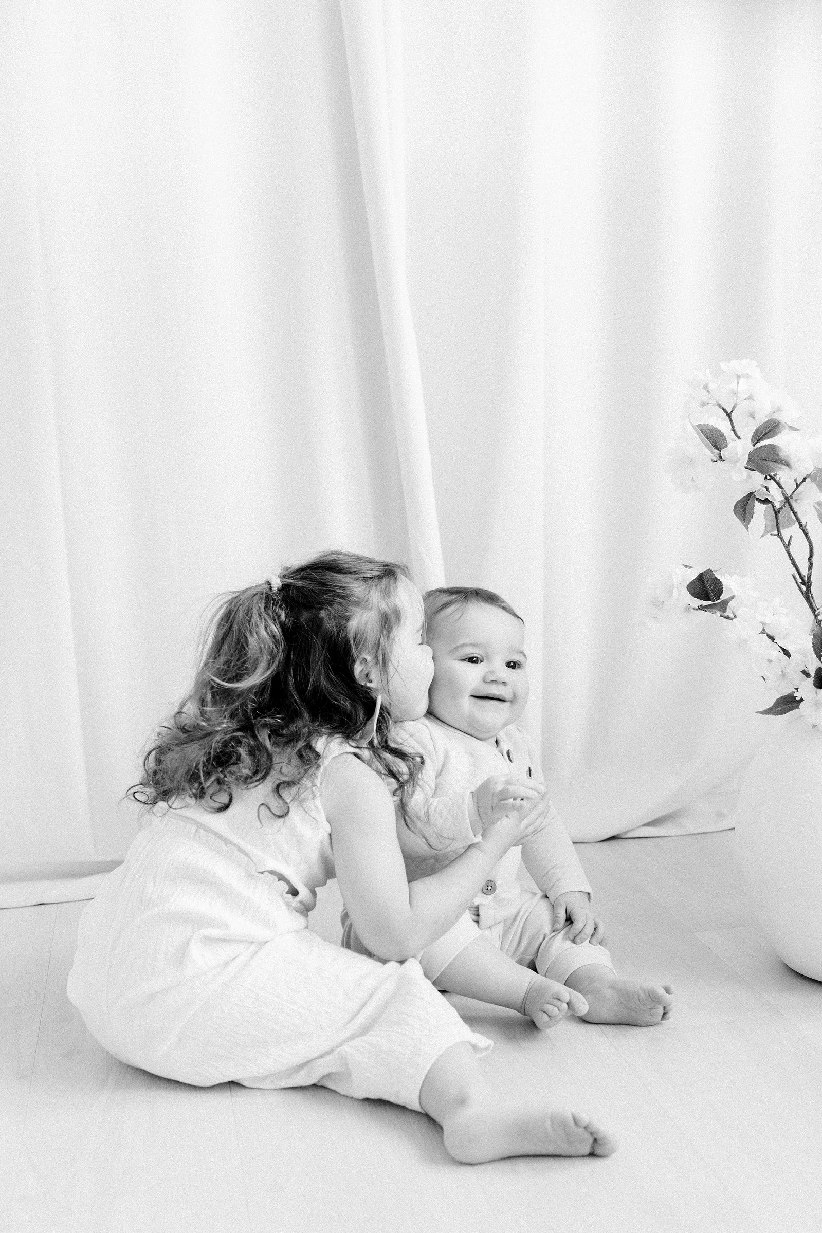 Black & white portrait of a big sister giving her baby brother a kiss on the cheek. Baby boy is laughing. Emily VanderBeek Photography. Ottawa family photographer. Candid photography.